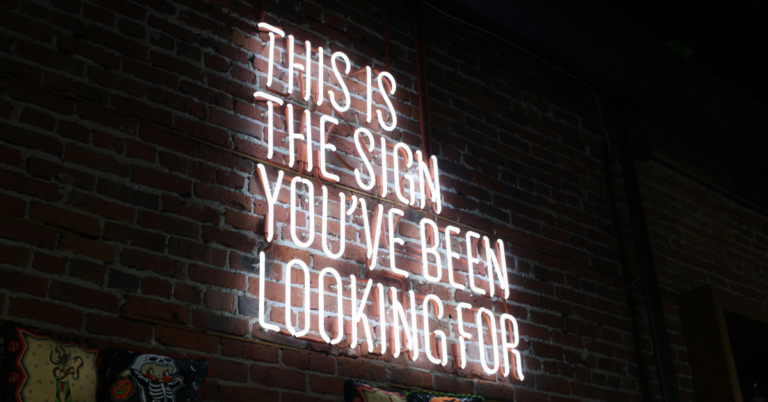 Neon sign on a brick wall reading 'This is the sign you've been looking for,' symbolizing the importance of target audience analysis, how to test a business idea, and hobby to business validation when validating a business idea.